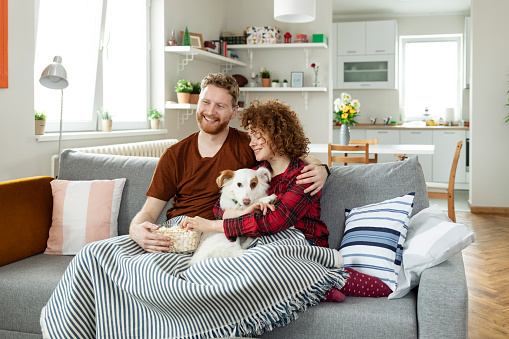 Happy Young Couple Watching Television at Home With Their Dog While Sitting on the sofa in the Living Room