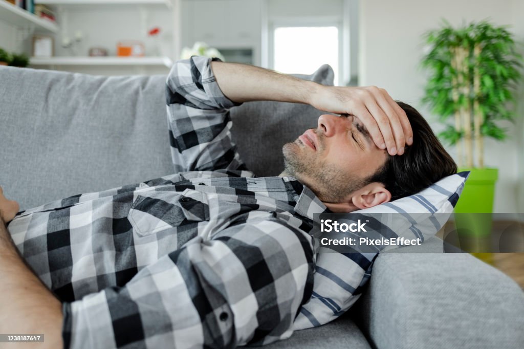 Headache's always hit you at the worst times Feeling Stressed. Frustrated Handsome Young Man Touching His Head and Keeping Eyes Closed on the Couch at Home While Having Headache Lying Down Stock Photo