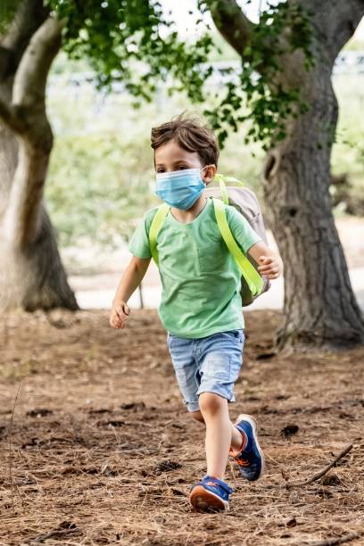 little boy running to school carrying a backpack in his shoulders wearing a protective face mask - little boys preschooler back to school backpack imagens e fotografias de stock