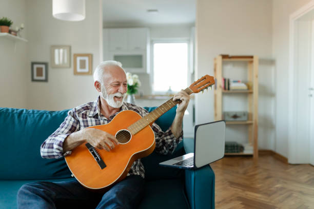 Elderly man learns to play acoustic guitar online using a Laptop