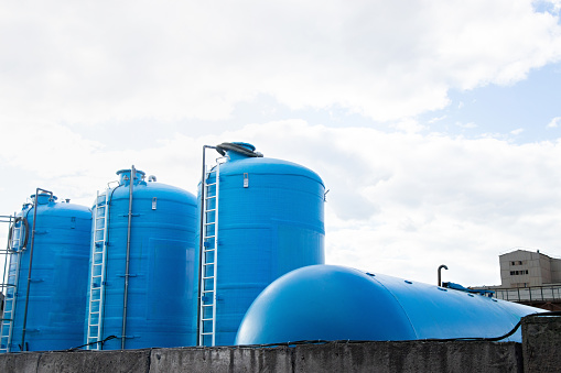 Row of blue round industrial containers on background of cloudy sky located on the territory of plant
