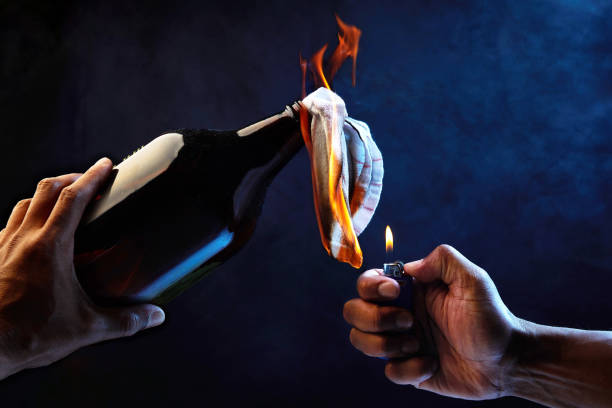 Studio image depicting riot hands holding and lighting the flame for a molotov cocktail with smoke background and blue lights representing police.