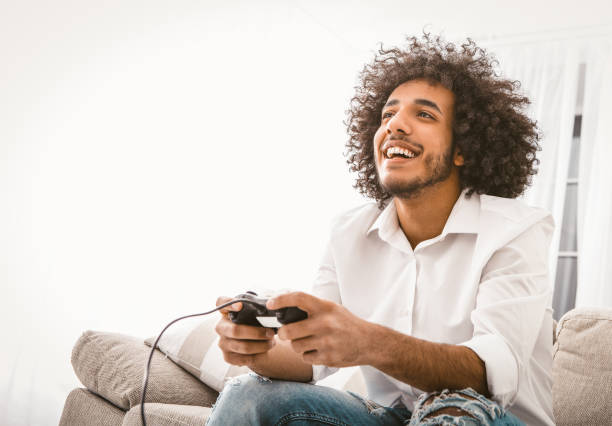 istock Happy man playing computer games. Young Arab guy entertains at home in self isolation during quarantine. Copy space at left side. Toned image 1238314743
