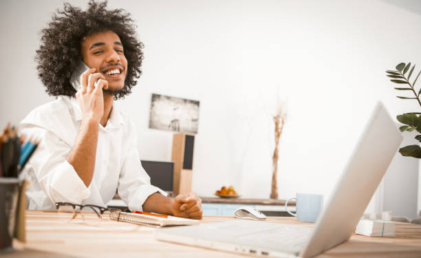istock Happy Arabic man talks on mobile phone toothy smiling. Creative entrepreneur communicates on smarthpone looking at camera while working from home. Copy space at right side. Toned image 1238337684