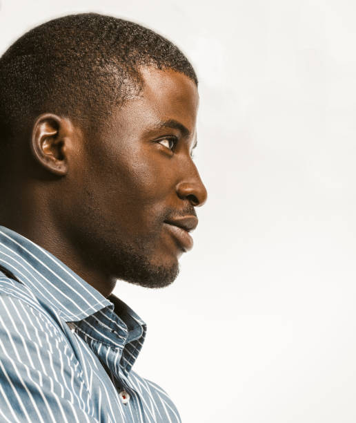 istock Confidently African American man delicately smiling looking at right side with textspace. Young dark-skinned businessman isolated on white background. Profile view. Close up bottom shot. Toned image 1238357886