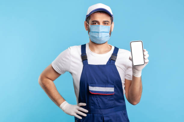 istock Worker in overalls and gloves holding mobile phone with blank display, device mock up for order app 1238385157