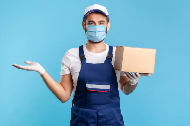 istock Happy worker in uniform carrying cardboard box and raising other hand to hold empty space 1238385167