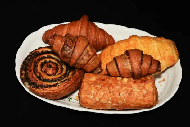 Breakfast -  porcelain platter  with Croissants, donuts, crullers  on black background