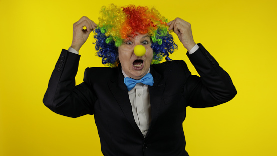 Holiday concept. A clown in a bright blue and yellow suit adjusts his glasses