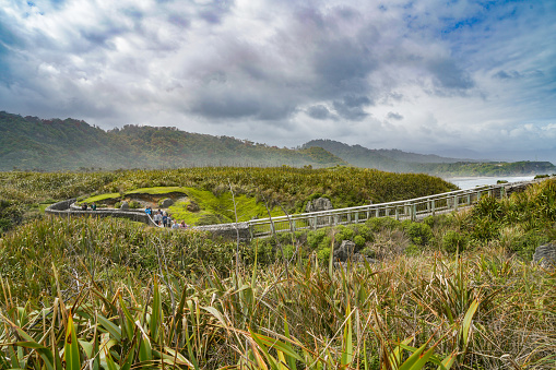 Tourists are walking on the wooden walkway enjoying view of Paparoa National Park, New Zealand.