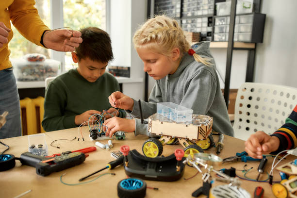 istock Quality and engineering. Young technicians building a robot, working with a wiring kit together with a male teacher at a stem robotics class. Inventions and creativity for kids 1238418890