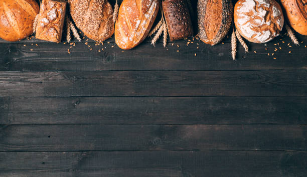 istock Bread border on black wood background with copy space. Composition of black, brown and white whole grain loaves with spikelets, still life. Panorama, banner. Bakery, cooking and grocery store concept. 1238470839
