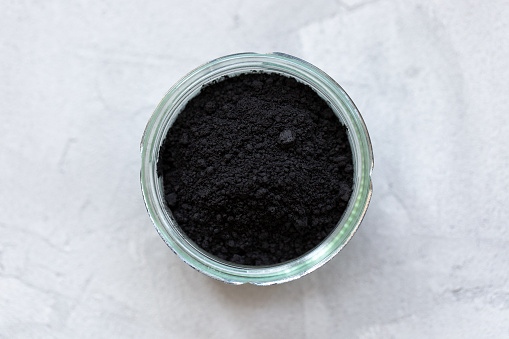 Black activated charcoal powder in a glass. Superfood, ingredient for cosmetics and vegan, vegetarian food, detox concept. Gray background. Copy space, selective focus