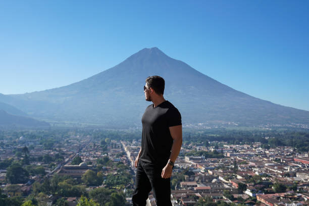 A young man with sunglasses posing safely in nature with a volcano on a sunny day