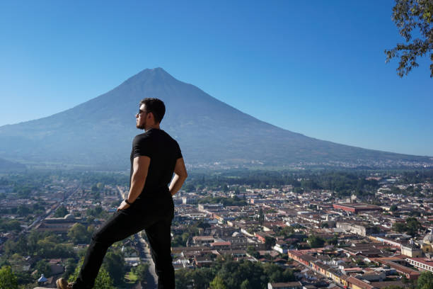 Young man with sunglasses observing the volcano and the city of Antigua Guatemala from the hill