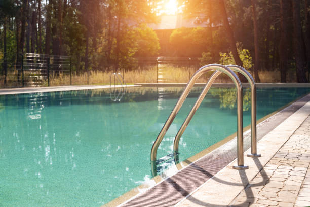 Big luxury empty rectangular swimming pool with clean blue water and ladder at tropical forest beach resort at sunrise morning light and nobody outdoors. Healthy leisure lifestyle travel and exercise