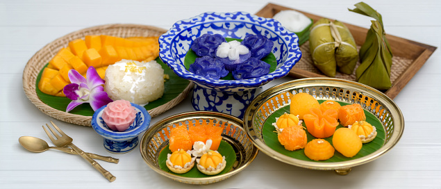 Close up view of several Thai traditional dessert serving on porcelain, wooden tray and brass tray with brass cutlery on plank table