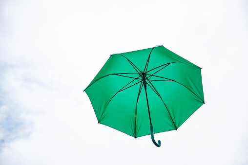 A green umbrella floats in the air with summer sky and clouds.