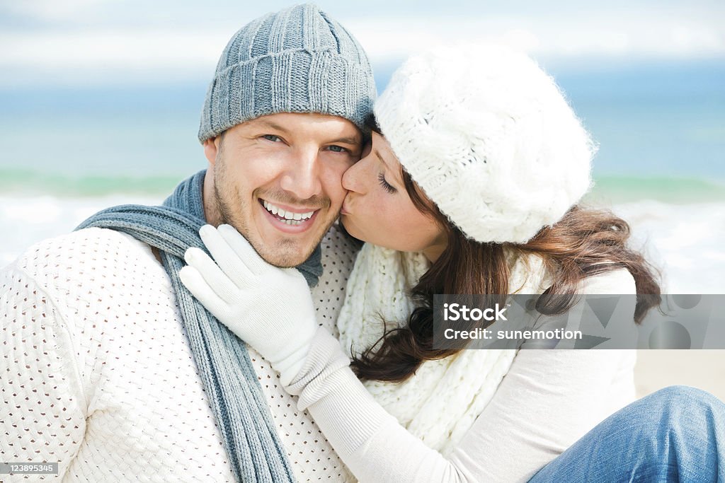 Joyful couple dressed in white and blue winter apparel young couple in warm clothes on the beach in colder season Adult Stock Photo