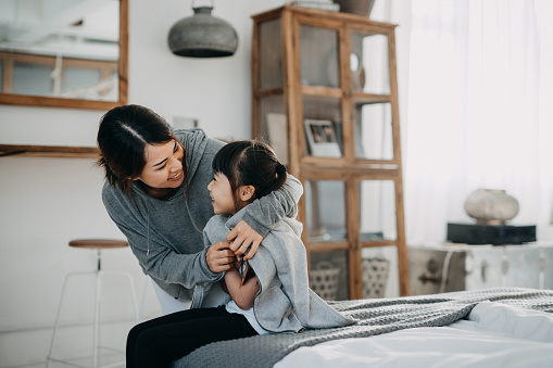 Cuidar a la joven madre asiática poniéndole un abrigo a su hija en casa photo