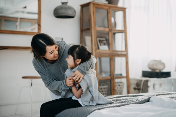 cuidar a la joven madre asiática poniéndole un abrigo a su hija en casa - aplicar fotos fotografías e imágenes de stock