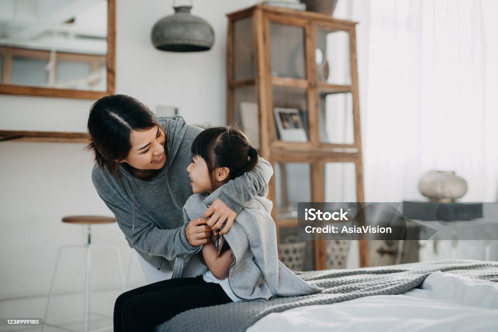 Caring young Asian mother putting a coat on her daughter at home Domestic Life Stock Photo