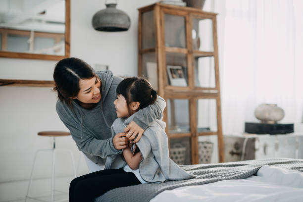 caring young asian mother putting a coat on her daughter at home - calca imagens e fotografias de stock