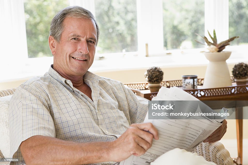 Hombre leyendo periódico sonriente sala de estar - Foto de stock de 60-69 años libre de derechos