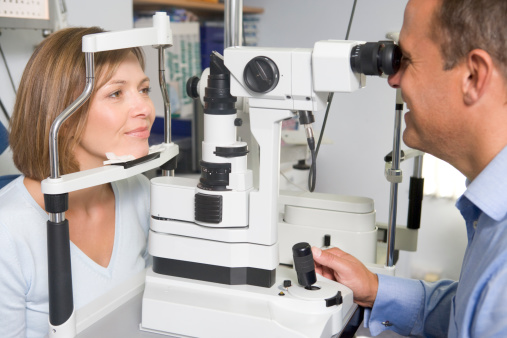 Optometrist in exam room with woman sitting in chair looking into eye test machine