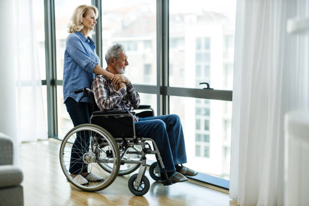 Mature woman and her disabled husband looking through window.