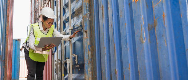 istock Black foreman woman worker working checking at Container cargo harbor holding laptop computer to loading containers. African dock female staff business Logistics import export shipping concept. 1239148028