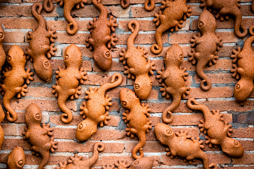 Group of gecko terracotta sculptures attached to orange brick wall as decorative items.