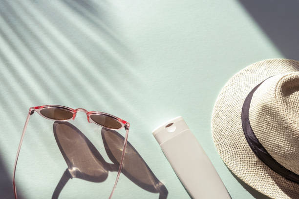 istock Sun hat, glasses and spf cream or lotion unbranded package on light blue background with palm tree leaf shadow, top view 1239164198