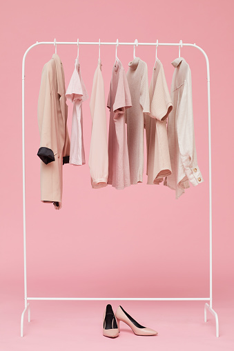 Image of sets of clothes hanging on hanger with shoes on the floor isolated on pink background