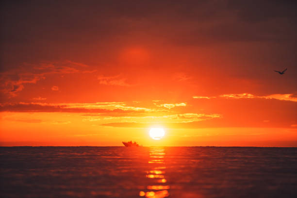Silhouette of two people in a local small fishing boat moving with sunrise in the background stock photo
