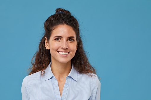 Portrait of young beautiful woman with curly hair smiling at camera isolated on blue background
