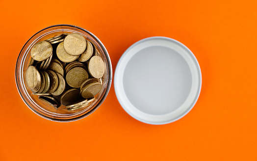 Glass jar full of coins on colored background.