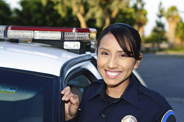 Friendly female Hispanic police officer a Hispanic police officer smiling next to her unit. police force smiling officer stock pictures, royalty-free photos & images