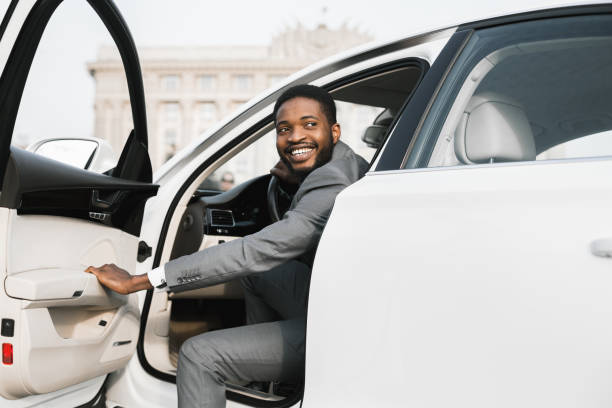 empresario abriendo puerta de automóviles saliendo del auto en la ciudad - alquiler de coche fotografías e imágenes de stock