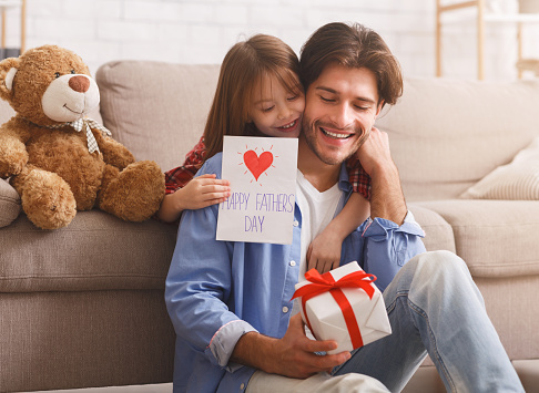 Happy Father Day, sweet girl surprising her daddy with gift and self-made card, happy dad holding gift box, copy space