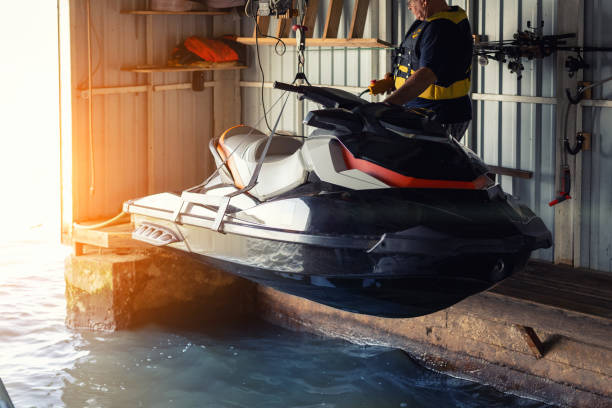 istock Senior man launching or lifting modern fast jetski hanged on strpas with wire hoist rail crane for dry storage. Boat garage interior for boats and jet-ski storage, service and maintenance 1239229579