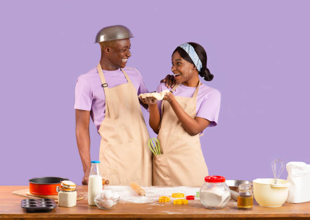 istock Cheerful black girlfriend and boyfriend enjoying their baking activity on lilac background 1239237018