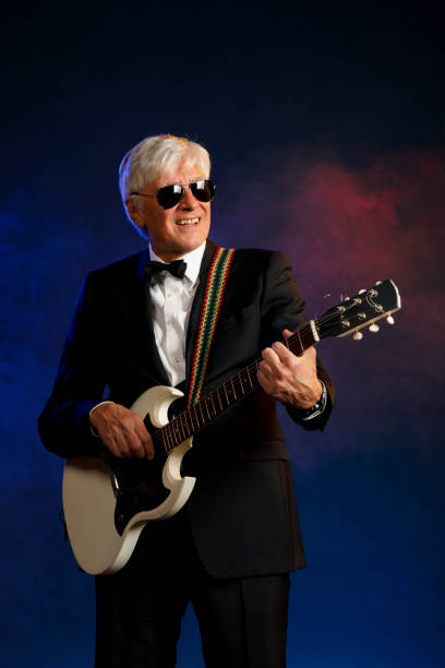 istock Musician Guitarist Active senior Handsome man playing guitar. Blue  background, with rays of light and special effects smoke. 1239243356