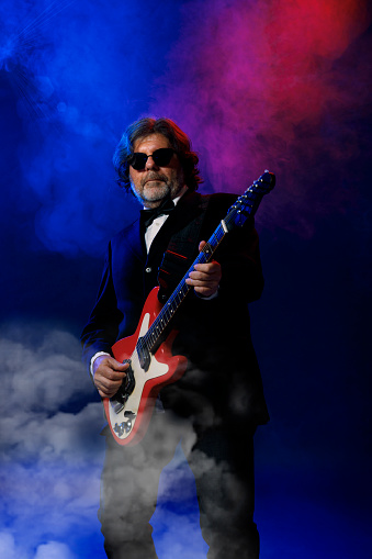 Musician Guitarist Active senior Handsome man playing guitar. Blue  background, with rays of light and special effects smoke.