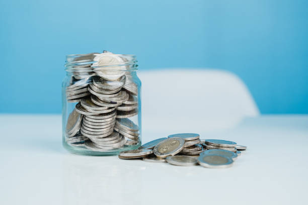 монеты в стеклянной банке с синим фоном, деньги и сохранение концепции. - making money фотографии стоковые фото и изображения