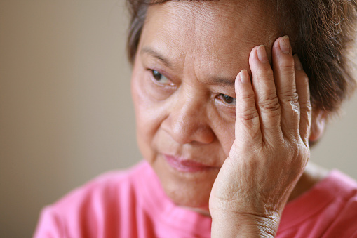 Elderly Asian woman with a worried look on her face, shallow depth of field with focus on hand.