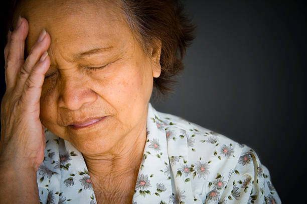 Distraught, pained older woman, eyes closed, hand to brow stock photo