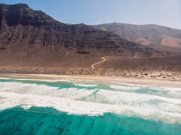 Aerial view of Famara beach, scenic landscape with ocean waves and mountains in Lanzarote, Canary islands Aerial view of Famara beach, scenic landscape with ocean waves and mountains in Lanzarote, Canary islands caleta de famara lanzarote stock pictures, royalty-free photos & images