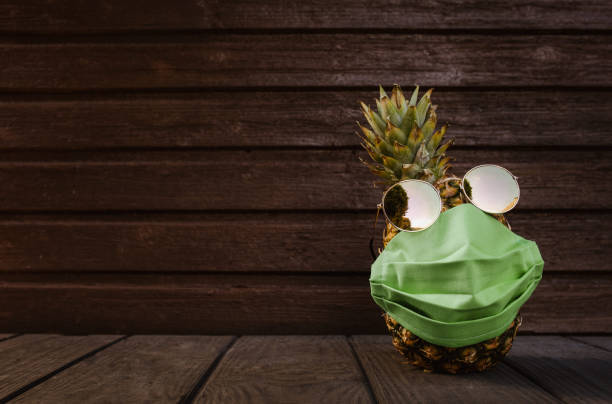 istock Pineapple face with face mask and sunglasses on and wooden background 1239315521