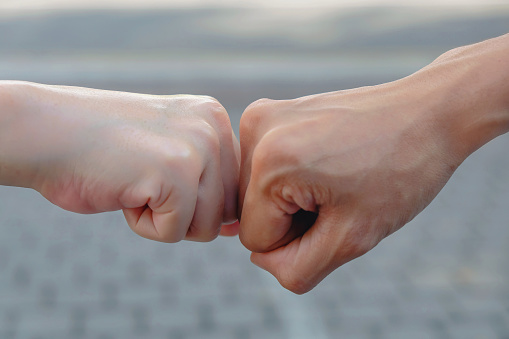 Close up shot of two friends doing fist bump on the street, during Covid 19 epidemic